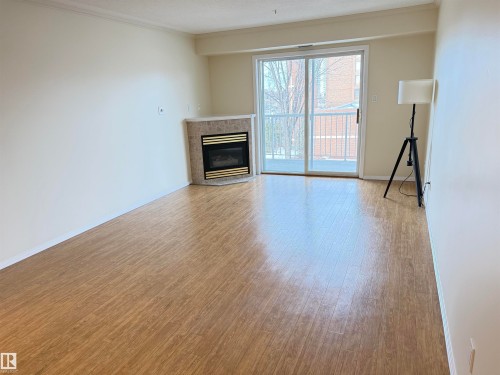 Unfurnished living room with light wood-style floors, crown molding, and a glass covered fireplace - 302 8215 84 Avenue, Edmonton, AB - Indoor Photo Showing Living Room With Fireplace