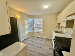 Kitchen with light countertops, white cabinetry, light wood finished floors, and black range with electric stovetop - 