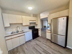 Kitchen with freestanding refrigerator, light countertops, black range with electric stovetop, dishwasher, and light wood-style floors - 