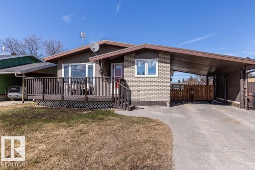 View of front facade featuring a wooden deck, brick siding, an attached carport, and driveway - 4628 46 Ave, Evansburg, AB - Outdoor With Deck Patio Veranda