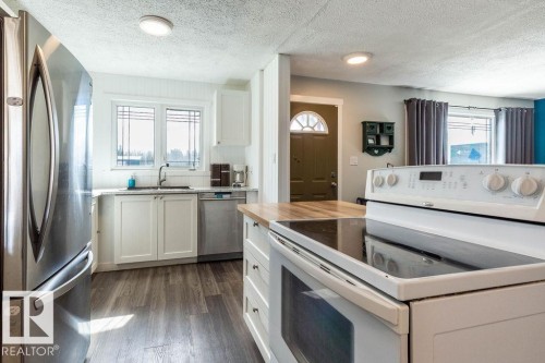Kitchen featuring stainless steel appliances, butcher block countertops, white cabinets, dark wood finished floors, and a textured ceiling - 4628 46 Ave, Evansburg, AB - Indoor Photo Showing Kitchen