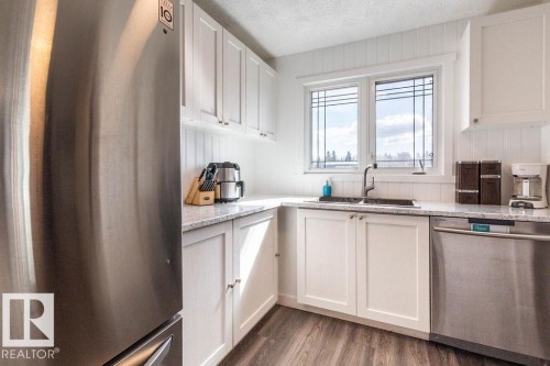 Kitchen featuring stainless steel appliances, a textured ceiling, white cabinetry, dark wood finished floors, and light stone countertops - 4628 46 Ave, Evansburg, AB - Indoor Photo Showing Kitchen With Double Sink