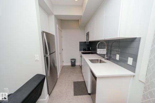 Kitchen featuring modern cabinets, white cabinetry, stainless steel appliances, tasteful backsplash, and light stone countertops - 70 446 Allard Boulevard, Edmonton, AB - Indoor Photo Showing Kitchen