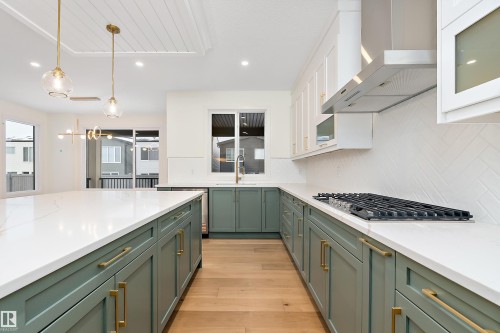 Kitchen with light wood finished floors, decorative light fixtures, two tone cabinetry, light stone countertops, and backsplash - Edmonton, AB - Indoor Photo Showing Kitchen With Upgraded Kitchen