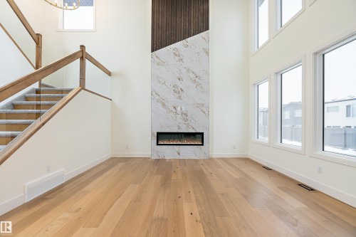 Unfurnished living room with a high ceiling, light wood-style flooring, healthy amount of natural light, and a premium fireplace - Edmonton, AB - Indoor With Fireplace
