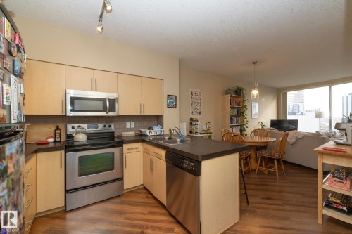 Kitchen with a peninsula, stainless steel appliances, open floor plan, dark countertops, and dark wood-style floors - 1004 10136 104 Street, Edmonton, AB - Indoor Photo Showing Kitchen With Stainless Steel Kitchen With Double Sink