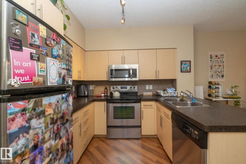 Kitchen featuring a peninsula, stainless steel appliances, dark countertops, dark wood finished floors, and tasteful backsplash - 1004 10136 104 Street, Edmonton, AB - Indoor Photo Showing Kitchen With Stainless Steel Kitchen With Double Sink