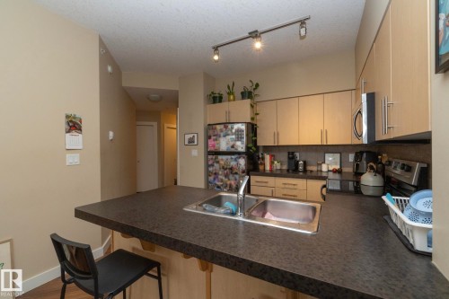 Kitchen with dark countertops, a peninsula, stainless steel appliances, a kitchen breakfast bar, and track lighting - 1004 10136 104 Street, Edmonton, AB - Indoor Photo Showing Kitchen With Double Sink