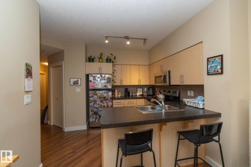 Kitchen with stainless steel appliances, backsplash, dark countertops, a peninsula, and a kitchen bar - 1004 10136 104 Street, Edmonton, AB - Indoor Photo Showing Kitchen With Double Sink