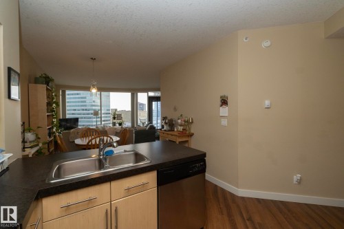 Kitchen featuring light wood finish cabinets, dark countertops, stainless steel dishwasher, open floor plan, and a textured ceiling - 1004 10136 104 Street, Edmonton, AB - Indoor Photo Showing Kitchen With Double Sink