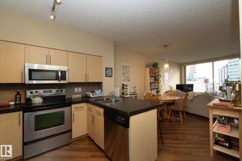 Kitchen with a peninsula, stainless steel appliances, dark countertops, open floor plan, and a textured ceiling - 1004 10136 104 Street, Edmonton, AB - Indoor Photo Showing Kitchen With Stainless Steel Kitchen With Double Sink