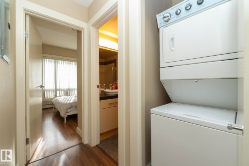 Laundry area featuring dark wood-style floors, stacked washing machine and dryer, and a baseboard heating unit - 1004 10136 104 Street, Edmonton, AB - Indoor Photo Showing Laundry Room