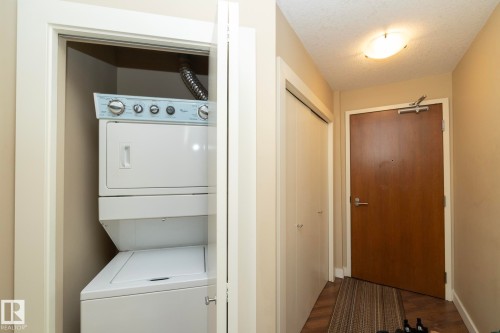Laundry area featuring a textured ceiling, stacked washer / dryer, and dark wood-type flooring - 1004 10136 104 Street, Edmonton, AB - Indoor Photo Showing Laundry Room