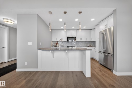 Kitchen with a kitchen breakfast bar, white cabinetry, stainless steel appliances, decorative light fixtures, and dark stone countertops - 416 61 Festival Way, Sherwood Park, AB - Indoor Photo Showing Kitchen With Upgraded Kitchen