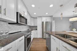 Kitchen with stainless steel appliances, light wood finished floors, dark stone countertops, and white cabinetry - 