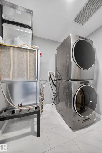 Laundry area featuring stacked washer and clothes dryer, heating unit, and light marble finish floors - 416 61 Festival Way, Sherwood Park, AB - Indoor Photo Showing Laundry Room