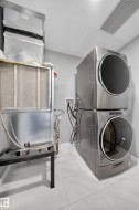 Laundry area featuring stacked washer and clothes dryer, heating unit, and light marble finish floors - 