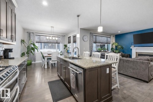 Kitchen featuring a kitchen bar, light stone counters, stainless steel appliances, open floor plan, and a textured ceiling - 14 Spring Bay, Spruce Grove, AB - Indoor Photo Showing Kitchen With Fireplace With Upgraded Kitchen