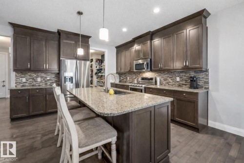 Kitchen featuring dark wood finish cabinetry, stainless steel appliances, light stone countertops, and a breakfast bar - 14 Spring Bay, Spruce Grove, AB - Indoor Photo Showing Kitchen With Double Sink With Upgraded Kitchen