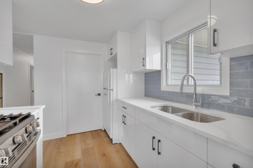 Kitchen with white cabinetry, light wood finished floors, stainless steel gas stove, light stone countertops, and freestanding refrigerator - 5021 46 Avenue, Calmar, AB - Indoor Photo Showing Kitchen With Double Sink