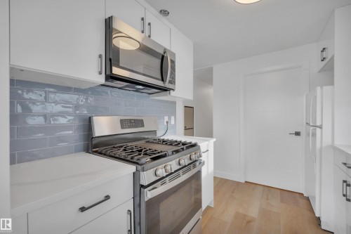 Kitchen featuring stainless steel appliances, white cabinets, light wood-style floors, backsplash, and light stone countertops - 5021 46 Avenue, Calmar, AB - Indoor Photo Showing Kitchen