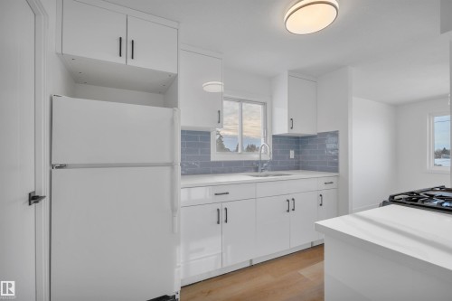 Kitchen with freestanding refrigerator, white cabinetry, light wood-type flooring, and decorative backsplash - 5021 46 Avenue, Calmar, AB - Indoor Photo Showing Kitchen