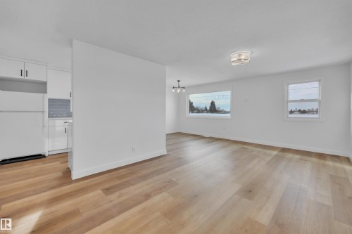 Empty room with a chandelier and light wood-style floors - 5021 46 Avenue, Calmar, AB - Indoor