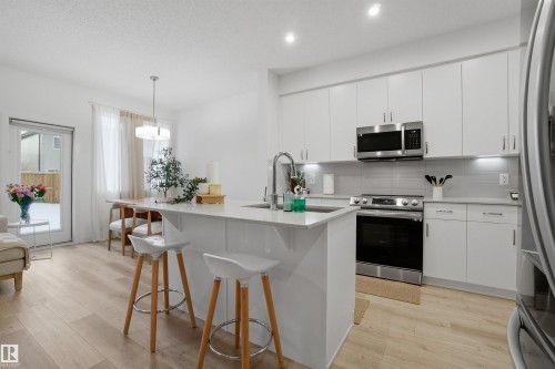 Kitchen featuring light wood-style flooring, stainless steel appliances, hanging light fixtures, and a center island with sink - 9882 225A St Nw, Edmonton, AB - Indoor Photo Showing Kitchen With Upgraded Kitchen