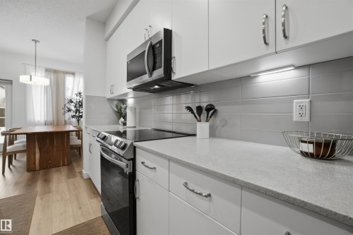 Kitchen with electric stove, white cabinetry, stainless steel microwave, tasteful backsplash, and light wood-style floors - 9882 225A St Nw, Edmonton, AB - Indoor Photo Showing Kitchen With Upgraded Kitchen