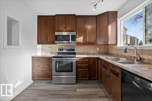 Kitchen with stainless steel appliances, dark wood finish cabinetry, dark wood-style floors, backsplash, and rail lighting - 133 Habitat Crescent, Edmonton, AB - Indoor Photo Showing Kitchen With Stainless Steel Kitchen With Double Sink