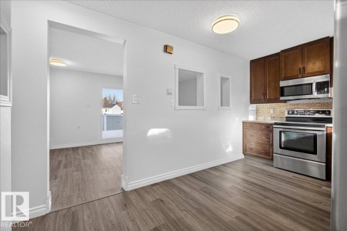Kitchen with stainless steel appliances, dark wood finish cabinetry, dark wood finished floors, decorative backsplash, and a textured ceiling - 133 Habitat Crescent, Edmonton, AB - Indoor Photo Showing Kitchen