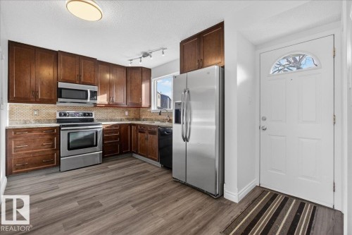 Kitchen featuring stainless steel appliances, a textured ceiling, dark wood finish cabinets, decorative backsplash, and dark wood-type flooring - 133 Habitat Crescent, Edmonton, AB - Indoor Photo Showing Kitchen With Stainless Steel Kitchen
