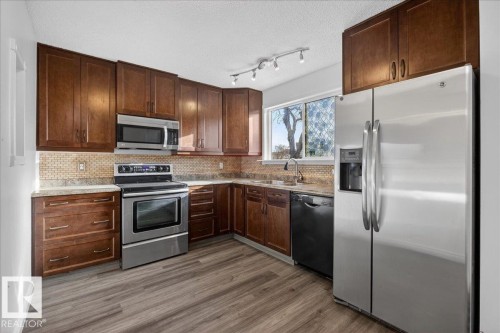 Kitchen featuring stainless steel appliances, a textured ceiling, dark wood finish cabinetry, dark wood-type flooring, and decorative backsplash - 133 Habitat Crescent, Edmonton, AB - Indoor Photo Showing Kitchen With Stainless Steel Kitchen