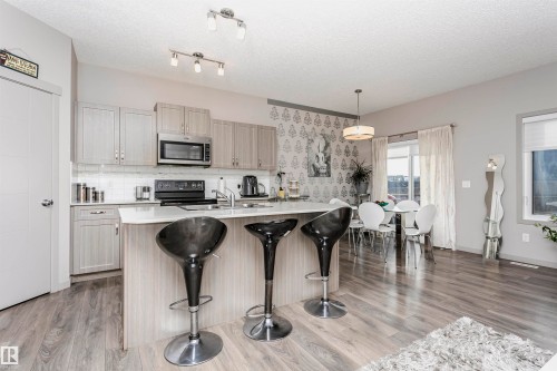 Kitchen with an island with sink, light wood-style floors, decorative light fixtures, a breakfast bar area, and a textured ceiling - 2855 16 Avenue, Edmonton, AB - Indoor Photo Showing Kitchen