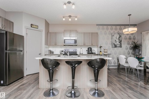 Kitchen featuring stainless steel appliances, a center island with sink, hanging light fixtures, a kitchen bar, and light wood finished floors - 2855 16 Avenue, Edmonton, AB - Indoor Photo Showing Kitchen