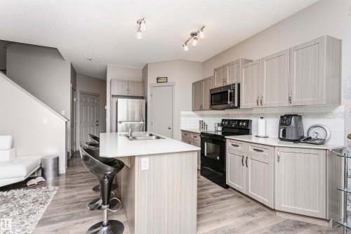 Kitchen featuring stainless steel appliances, a kitchen breakfast bar, a kitchen island with sink, light wood-style flooring, and backsplash - 2855 16 Avenue, Edmonton, AB - Indoor Photo Showing Kitchen