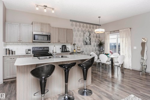 Kitchen with a kitchen bar, stainless steel microwave, a kitchen island with sink, dark wood finished floors, and range with electric stovetop - 2855 16 Avenue, Edmonton, AB - Indoor Photo Showing Kitchen With Double Sink