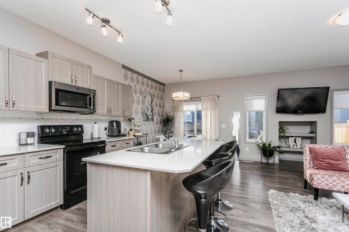 Kitchen with black range with electric stovetop, a textured ceiling, open floor plan, stainless steel microwave, and a kitchen bar - 2855 16 Avenue, Edmonton, AB - Indoor Photo Showing Kitchen With Fireplace With Double Sink