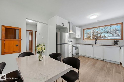 Kitchen with stainless steel appliances, white cabinetry, light wood-style floors, and a kitchen bar - 6007 95 Avenue, Edmonton, AB - Indoor