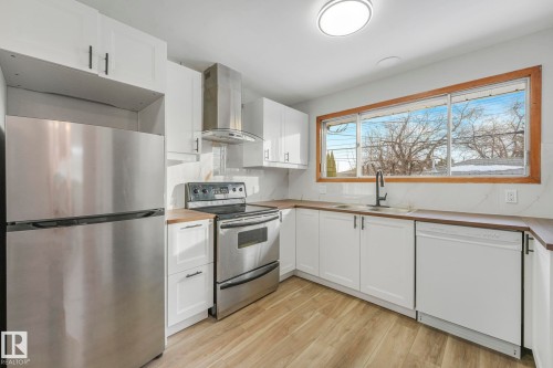 Kitchen featuring stainless steel appliances, extractor fan, white cabinets, light wood-type flooring, and wood counters - 6007 95 Avenue, Edmonton, AB - Indoor Photo Showing Kitchen