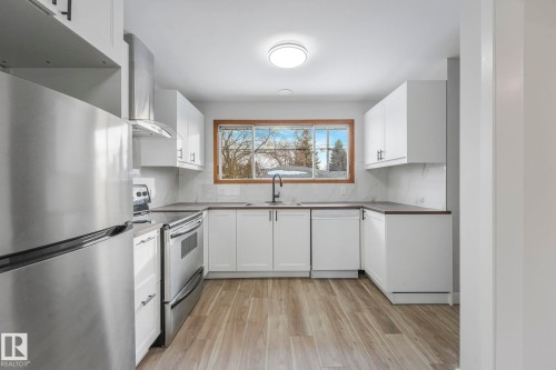 Kitchen with stainless steel appliances, light wood-type flooring, and white cabinetry - 6007 95 Avenue, Edmonton, AB - Indoor Photo Showing Kitchen With Double Sink