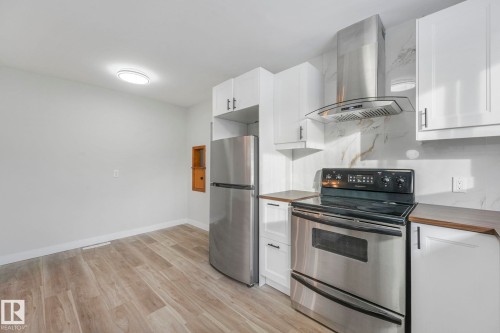 Kitchen with stainless steel appliances, exhaust hood, white cabinets, and light wood-type flooring - 6007 95 Avenue, Edmonton, AB - Indoor Photo Showing Kitchen