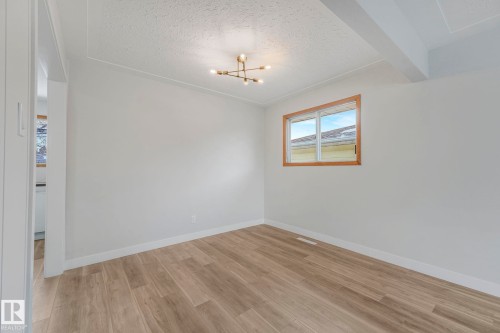 Empty room with light wood finished floors, a textured ceiling, and suspended lighting - 6007 95 Avenue, Edmonton, AB - Indoor Photo Showing Other Room