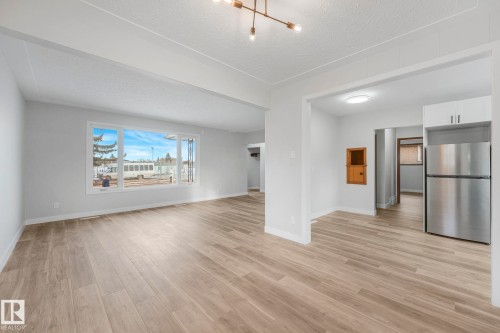 Unfurnished living room featuring a textured ceiling, light wood-style floors, and a chandelier - 6007 95 Avenue, Edmonton, AB - Indoor
