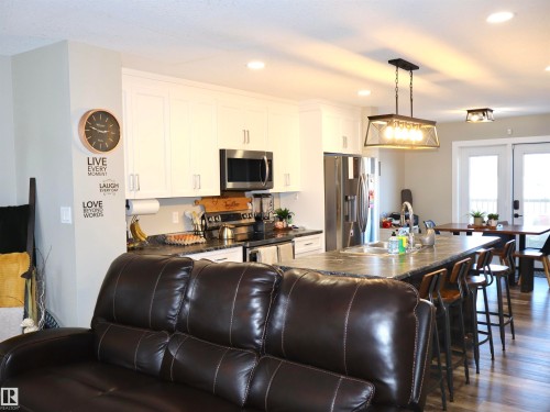 Kitchen with stainless steel appliances, dark wood finished floors, white cabinets, hanging light fixtures, and a breakfast bar - 9760 - 107 Street, Westlock, AB - Indoor