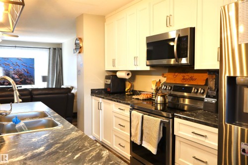 Kitchen featuring stainless steel appliances, dark stone countertops, white cabinetry, and open floor plan - 9760 - 107 Street, Westlock, AB - Indoor Photo Showing Kitchen With Double Sink