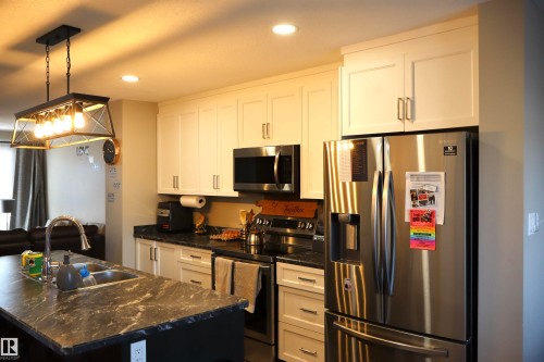 Kitchen with stainless steel appliances, white cabinetry, hanging light fixtures, dark stone counters, and a center island with sink - 9760 - 107 Street, Westlock, AB - Indoor Photo Showing Kitchen With Double Sink