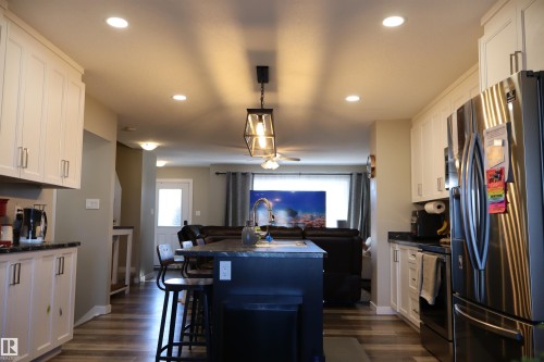 Kitchen with dark countertops, stainless steel appliances, open floor plan, a kitchen breakfast bar, and a kitchen island with sink - 9760 - 107 Street, Westlock, AB - Indoor Photo Showing Kitchen