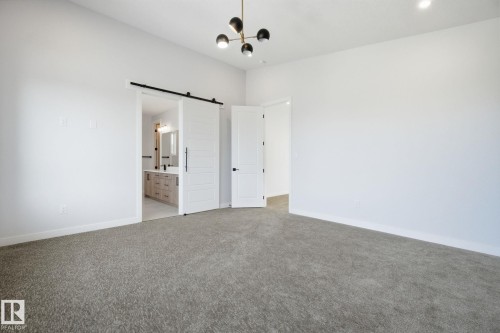 Unfurnished bedroom featuring a barn door, light carpet, ensuite bath, and suspended lighting - 17108 2 Street, Edmonton, AB - Indoor Photo Showing Other Room