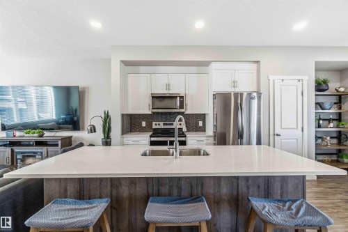 Kitchen with a kitchen bar, stainless steel appliances, white cabinetry, light stone countertops, and open floor plan - 1908 25 Street, Edmonton, AB - Indoor Photo Showing Kitchen With Stainless Steel Kitchen With Double Sink With Upgraded Kitchen